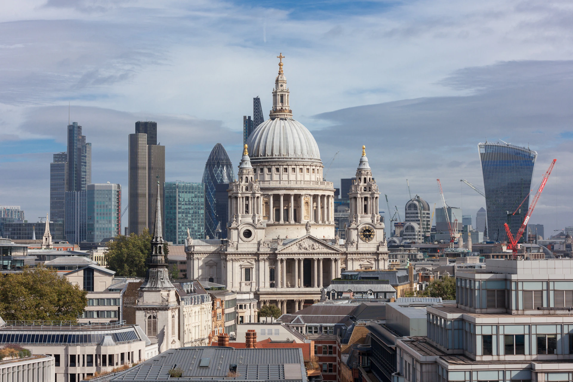 View of St. Paul's Cathedral in London, with modern skyscrapers and urban buildings in the background under a cloudy sky.