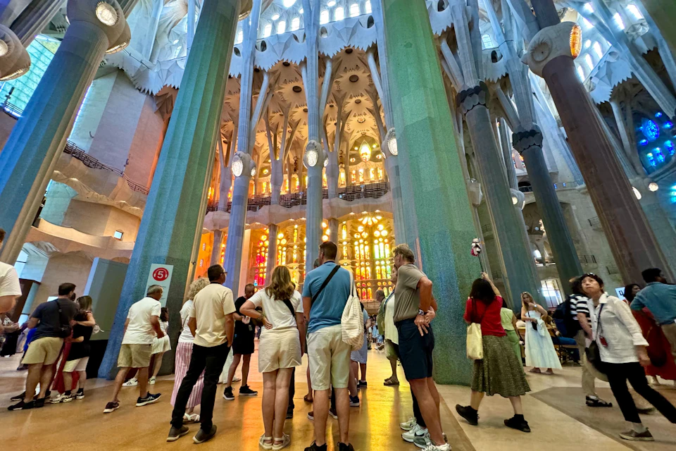 A group of people standing inside a large, ornate cathedral with tall columns and colorful stained glass windows.