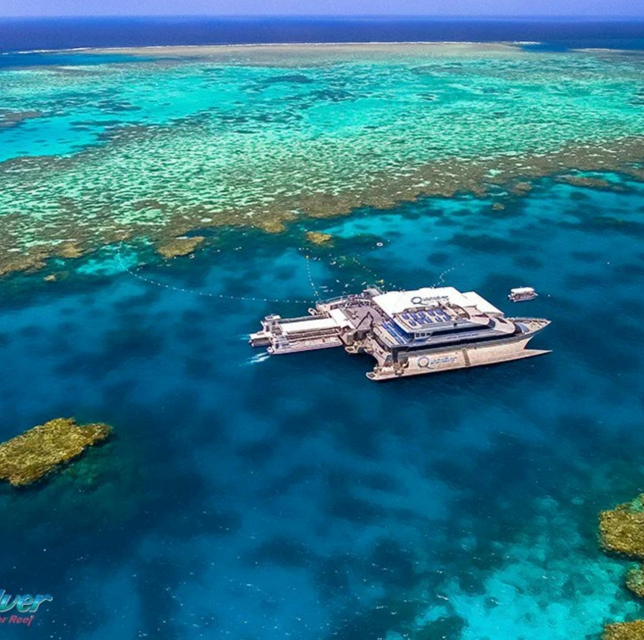 Aerial view of a floating platform and boats on the clear blue waters of a coral reef.