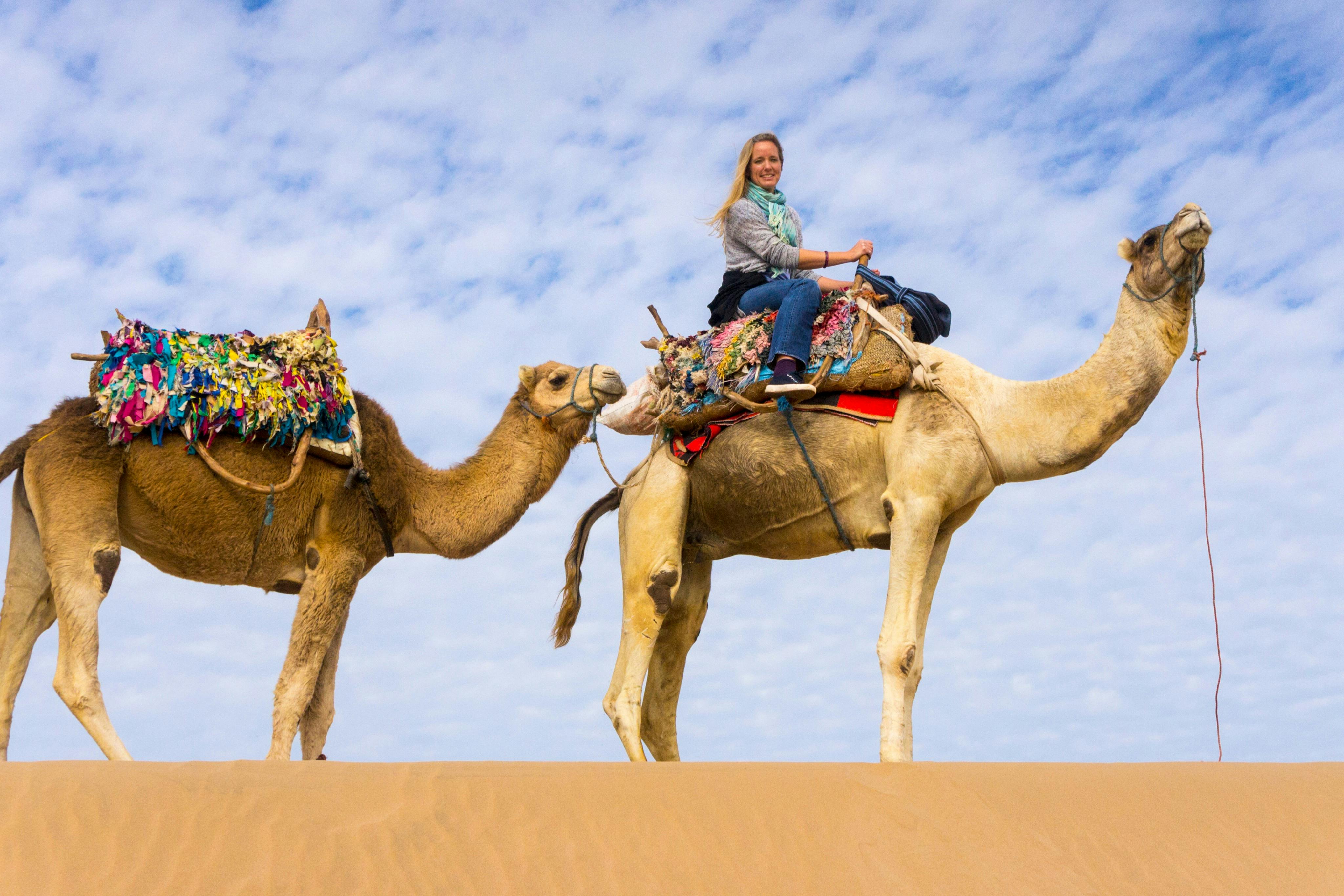 Una persona està muntant un camell en un desert amb un cel blau i núvols, acompanyada d&#39;un altre camell lligat al darrere.