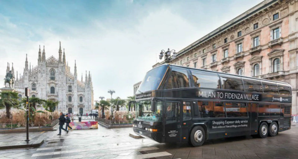 Double-decker bus with "Milan to Florence" text parked near a historic building and a cathedral in a city plaza.