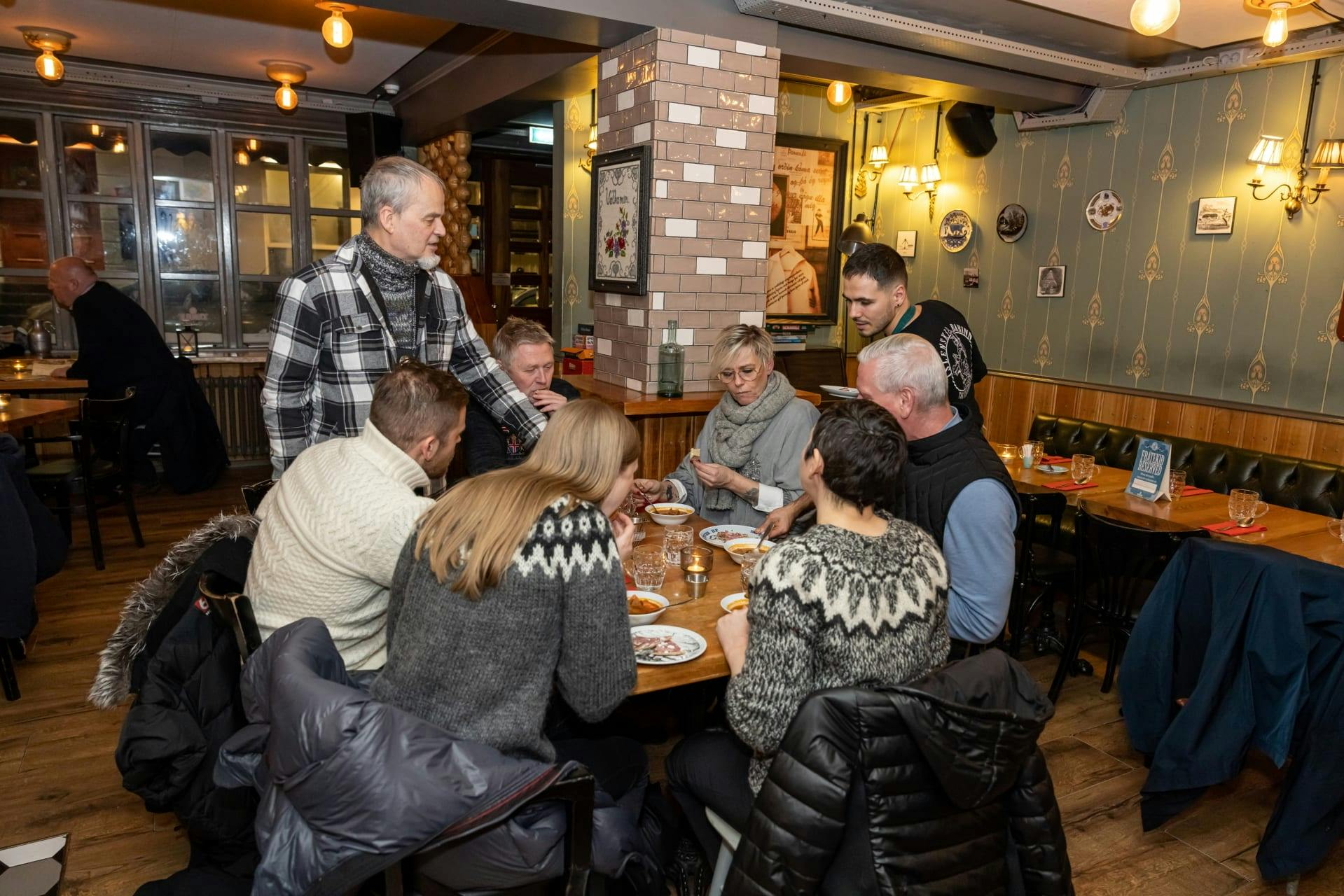 A group of people in cozy sweaters are gathered around a table enjoying a meal in a warmly lit restaurant.