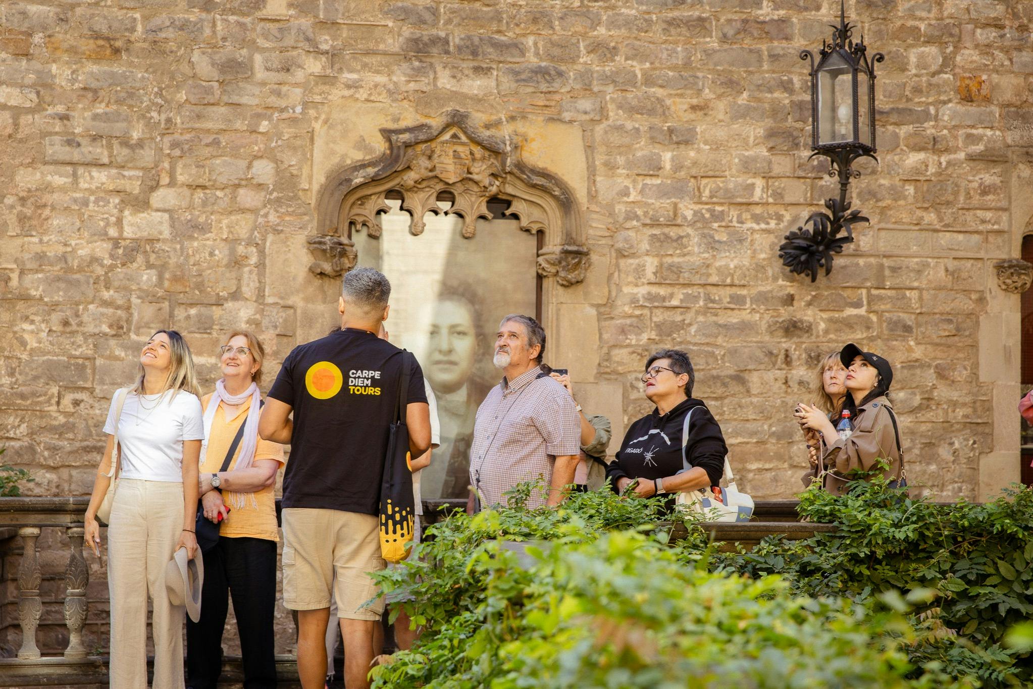 Un groupe de personnes participant à une visite guidée se tient près d'un mur de pierre orné, avec un cadre de fenêtre décoratif à l'arrière-plan.
