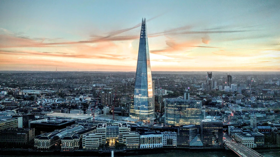 Cityscape featuring The Shard skyscraper at sunset with surrounding buildings and a river in the foreground.