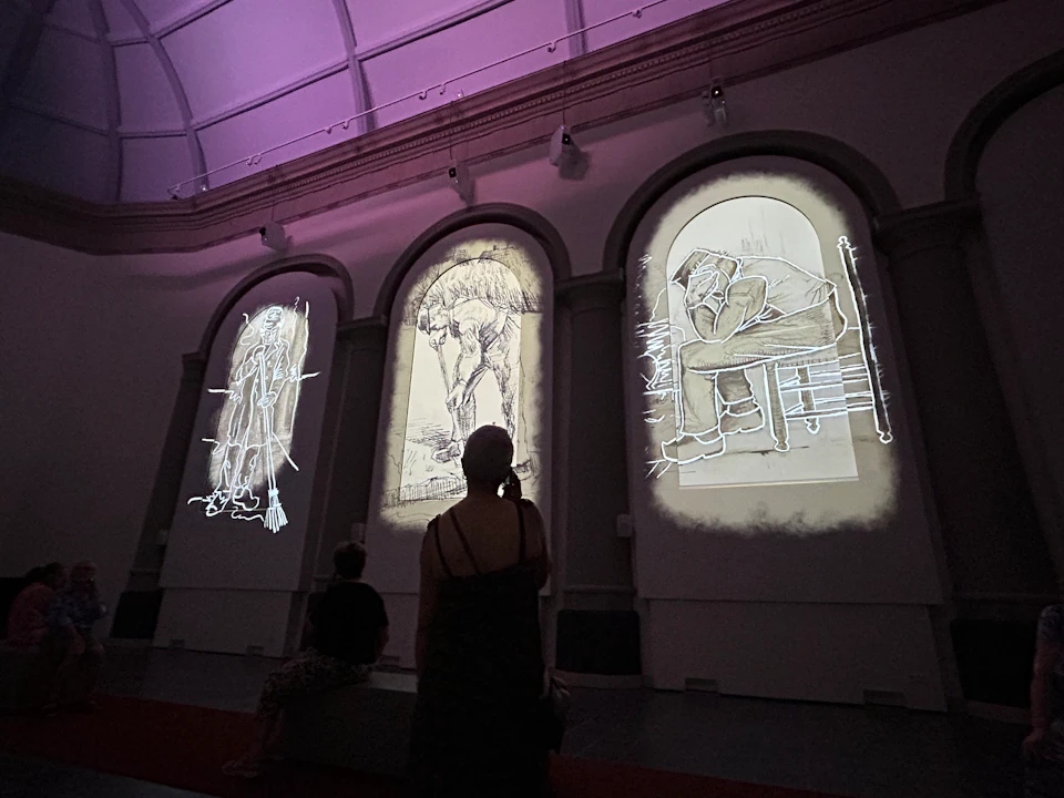 People viewing large, illuminated sketches projected on three tall, arch-shaped panels in an art gallery.