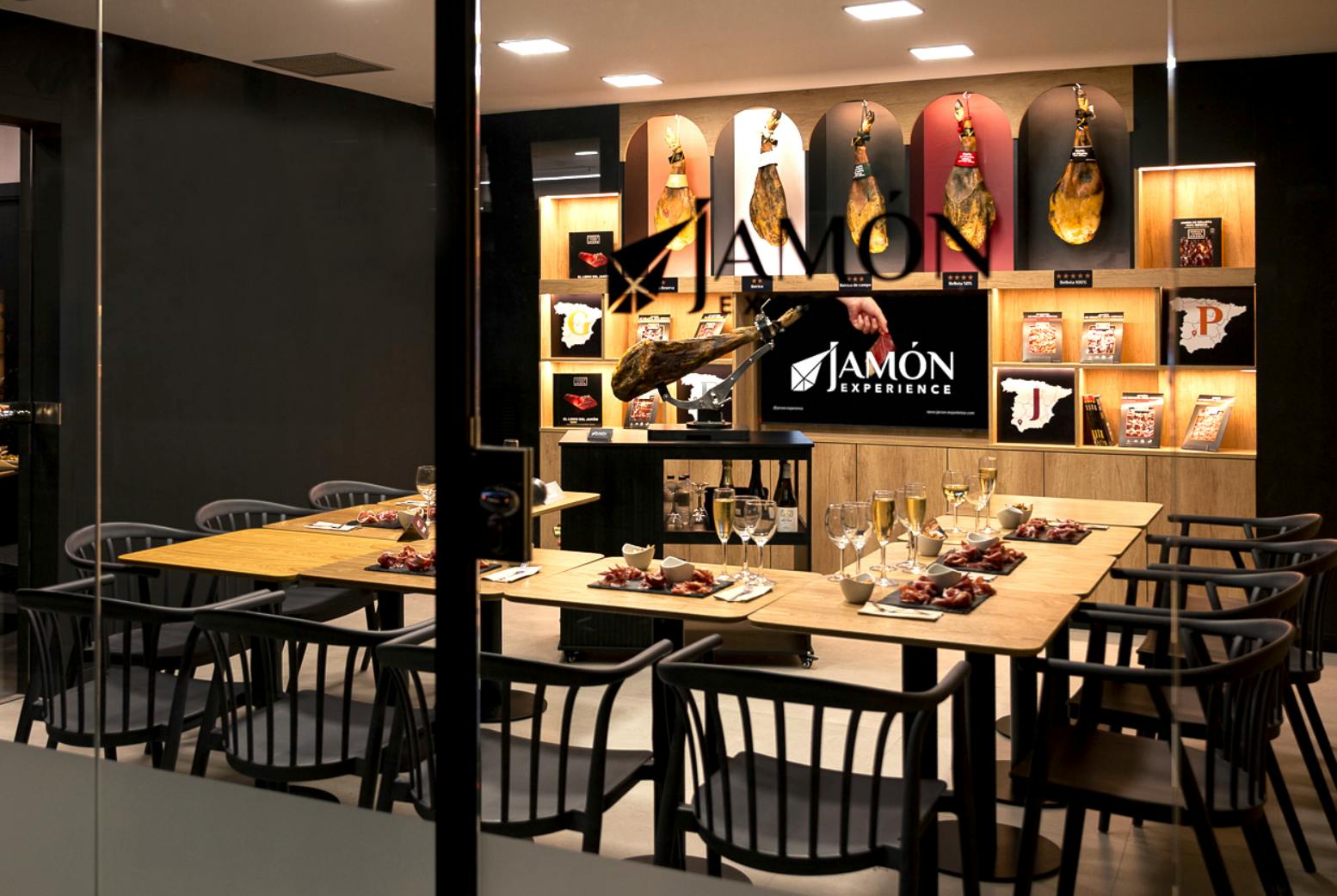 Uma área de refeições com mesas preparadas para uma refeição, um balcão com carnes curadas e uma placa que diz "Jamón Experience".