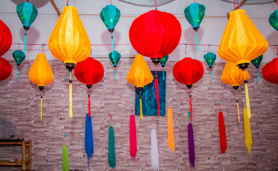 Colorful paper lanterns and hanging decorations against a textured wall.