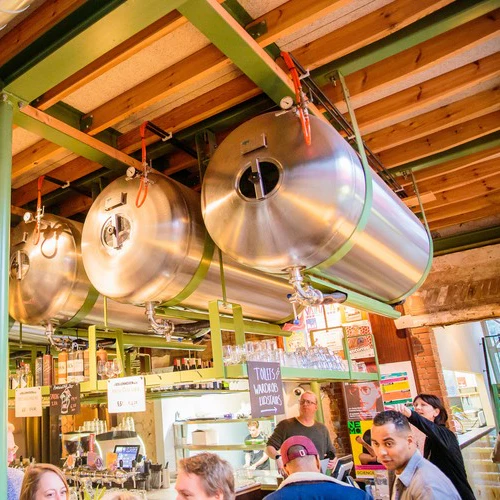 Bryggeriscen med stora tankar i rostfritt stål upphängda i taket och människor som umgås i baren nedanför.