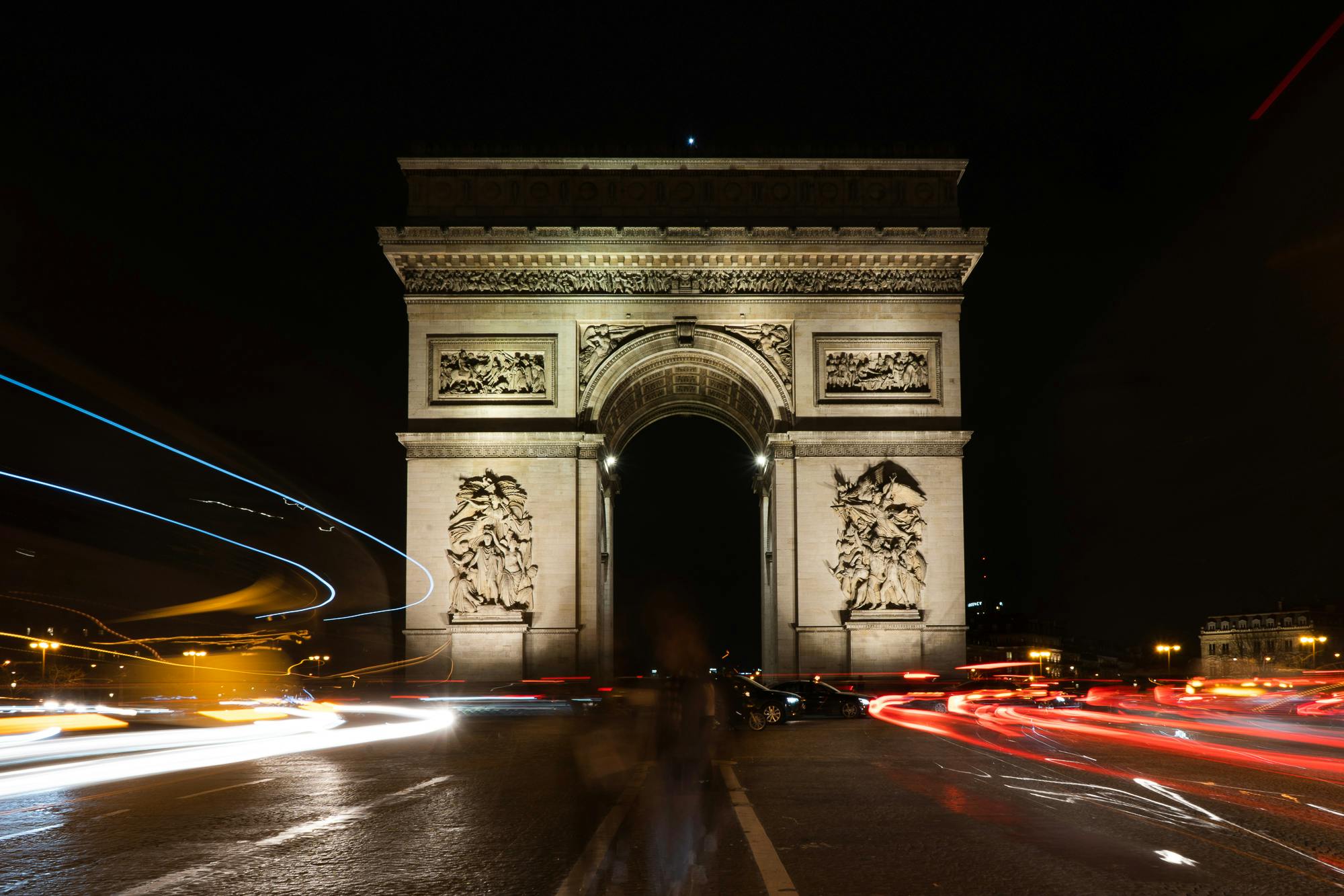 Long-exposure shot of the Arc de Triomphe at night with light trails from cars