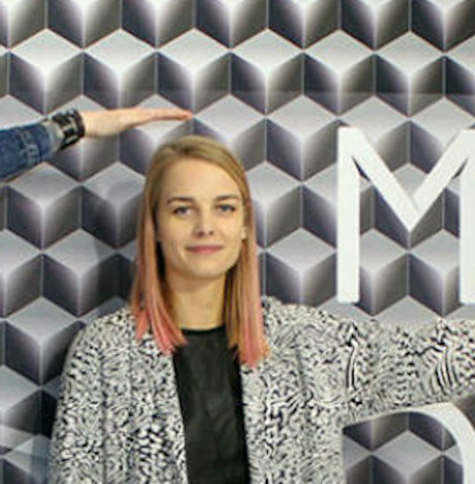 Three people standing in a room with an optical illusion. The background has geometric patterns and partially visible text.