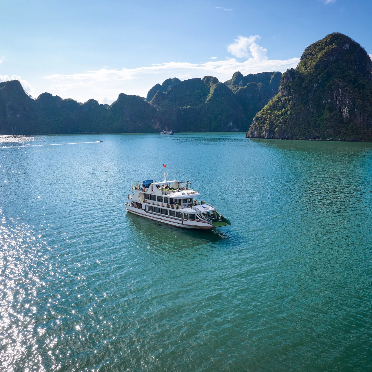 Boat sailing on calm turquoise water surrounded by lush, rocky islands under a clear blue sky.