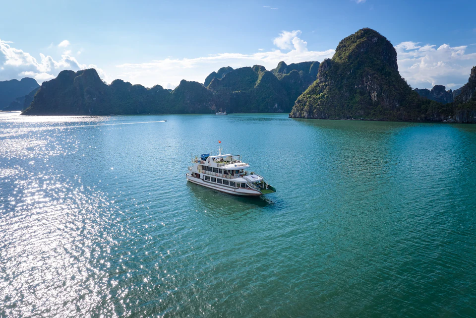 Boat sailing on calm turquoise water surrounded by lush, rocky islands under a clear blue sky.