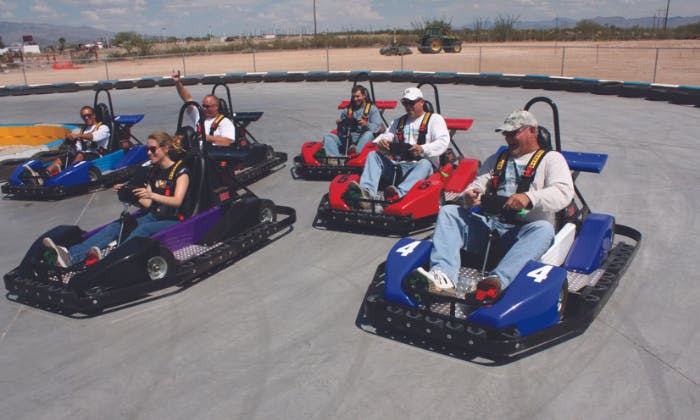 Pět lidí v motokárách na venkovní dráze se zaměřením na barevná vozidla a ležérní oblečení. Znečištěná oblast v pozadí.
