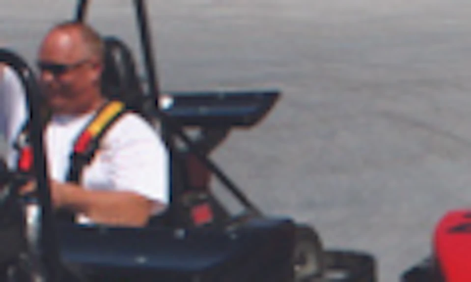 Five people in go-karts on an outdoor track, focusing on their colorful vehicles and casual attire. Dirt area in the background.