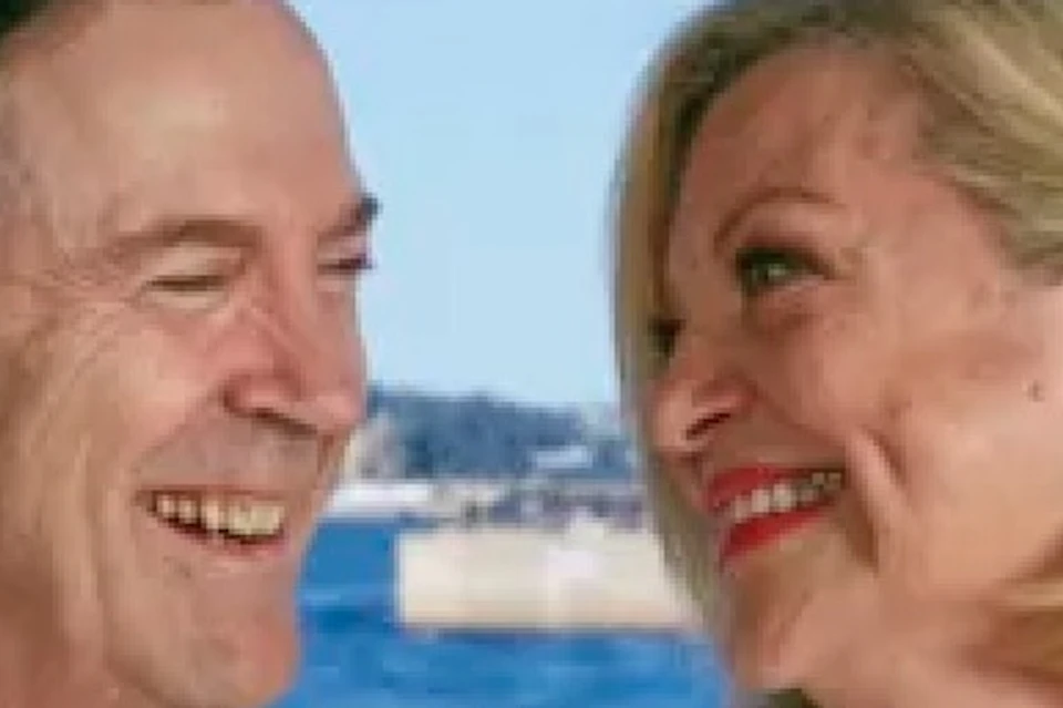 A couple smiling and holding champagne glasses at a table with coffee cups, with the Sydney Opera House visible in the background.