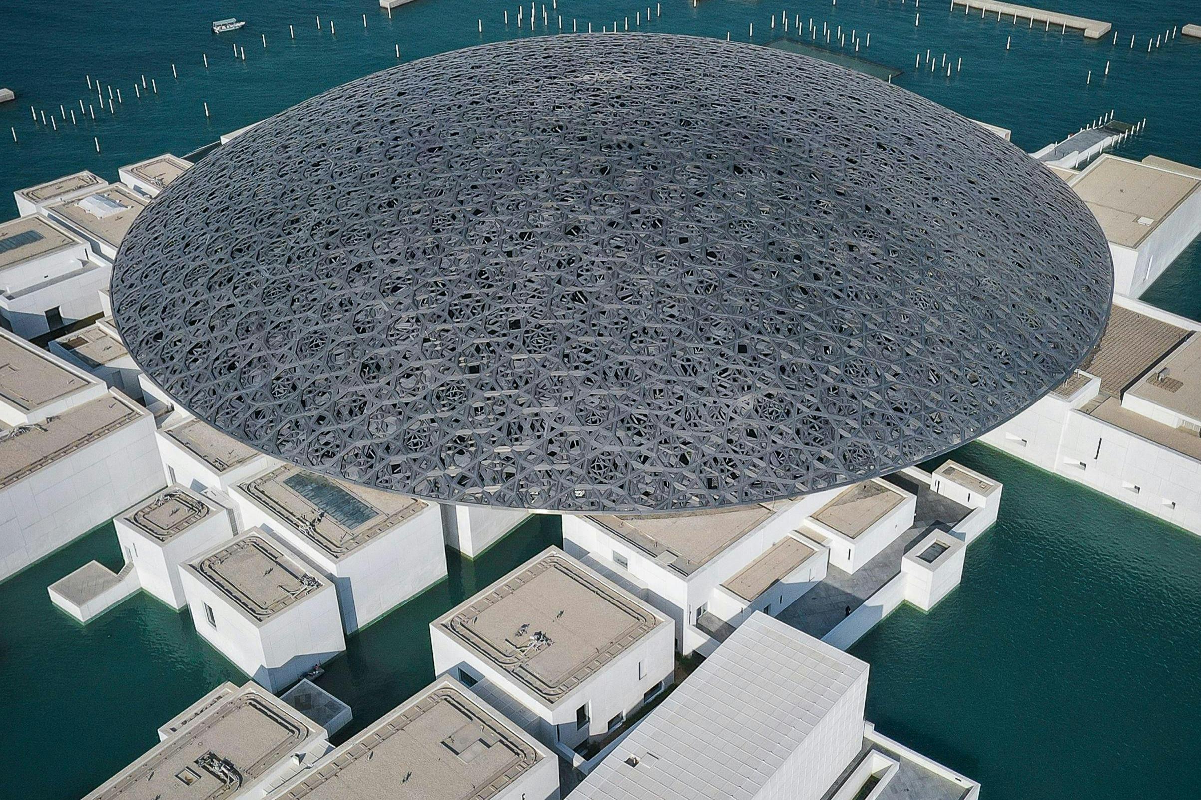 물로 둘러싸인 흰색 건물 위의 크고 복잡한 돔 구조의 공중 전망.