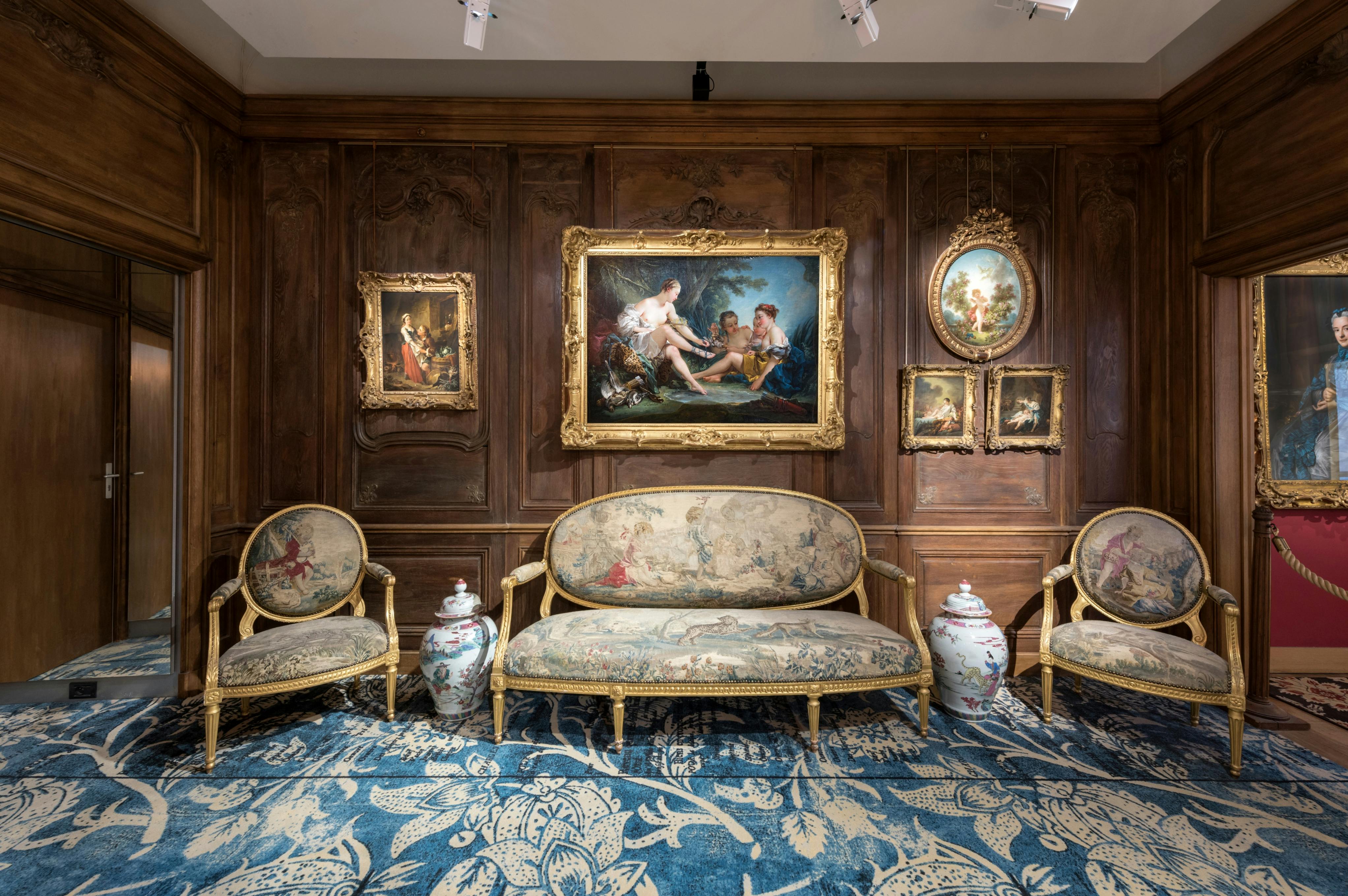 客厅装饰华丽，配有古董家具、框架画和装饰花瓶，地毯上有蓝色图案，墙壁上有木板。