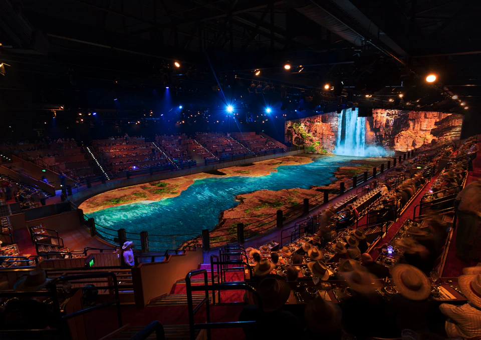 Large indoor theater with tiered seating and a stage featuring a vivid projection of a waterfall and river landscape.
