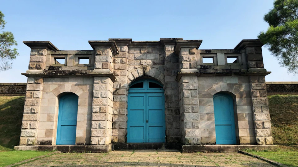 A stone building with three blue doors under a clear sky.