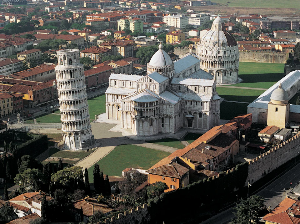 Aerial view of the Leaning Tower of Pisa, Pisa Cathedral, and Baptistery, surrounded by buildings and greenery.