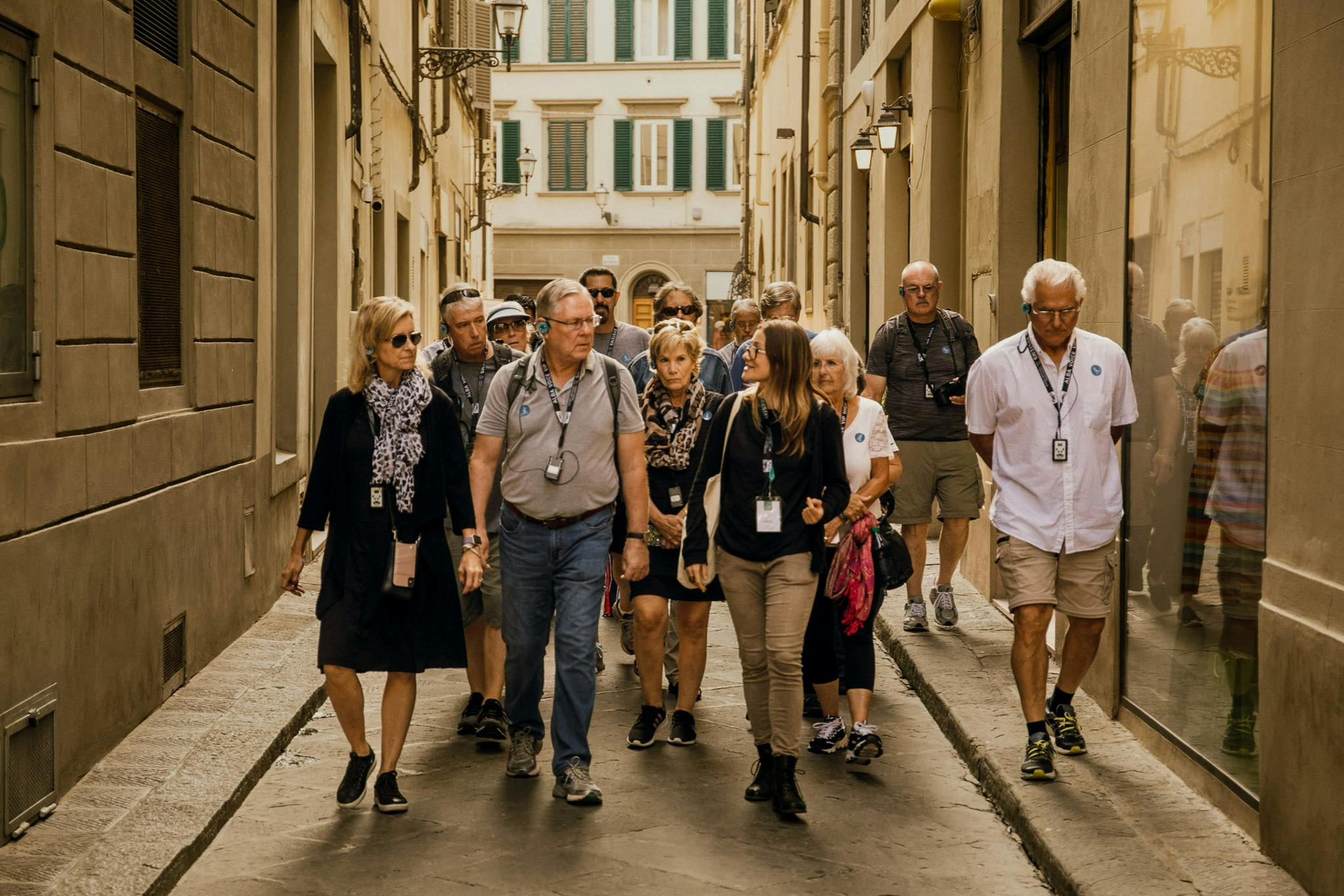 A group of people walking through a narrow street with tall buildings on both sides, appearing to be on a guided tour.