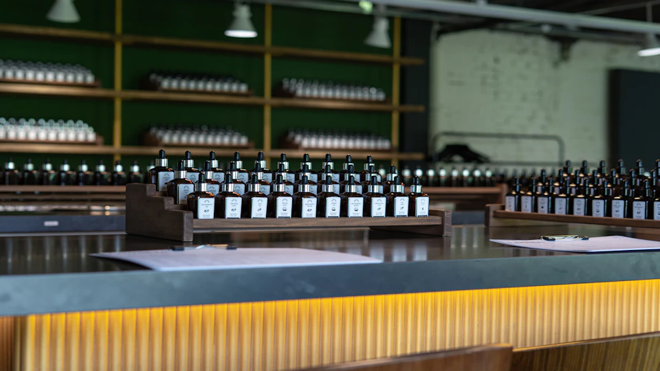 A countertop displaying rows of small bottles with labels, with shelves of similar bottles in the background.