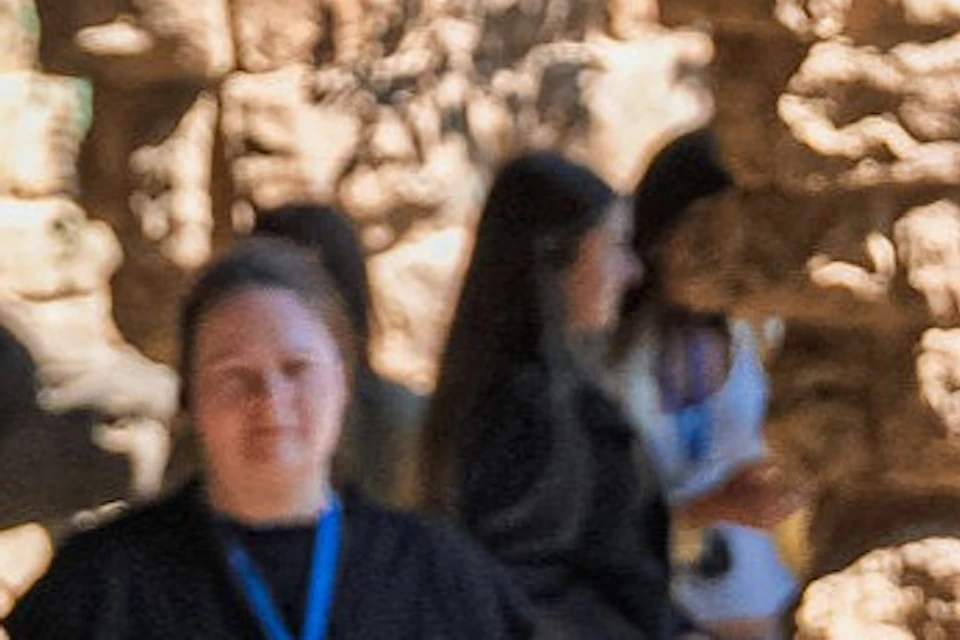 A group of people standing and talking near stone arches in an outdoor setting under sunlight.