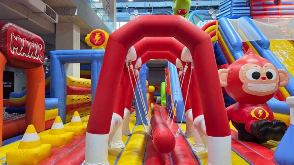 A colorful inflatable obstacle course with red, yellow, and blue sections in an indoor setting.