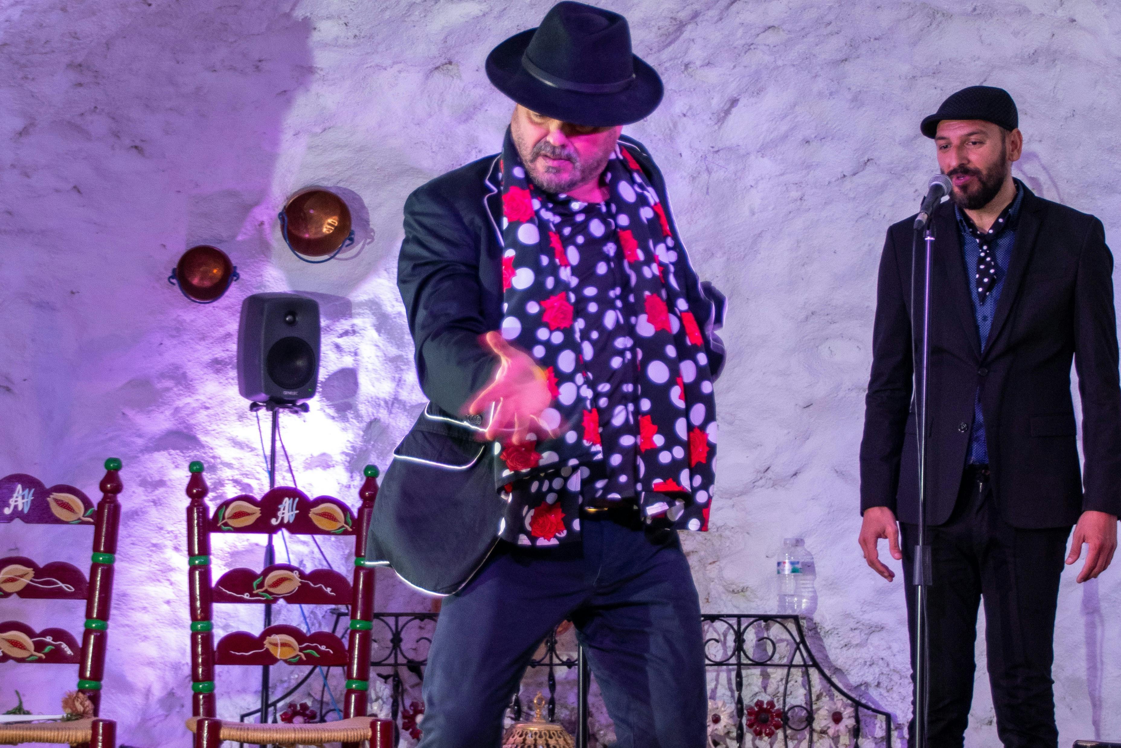 Two men perform on a stage; one is gesturing expressively, and the other stands behind a microphone.