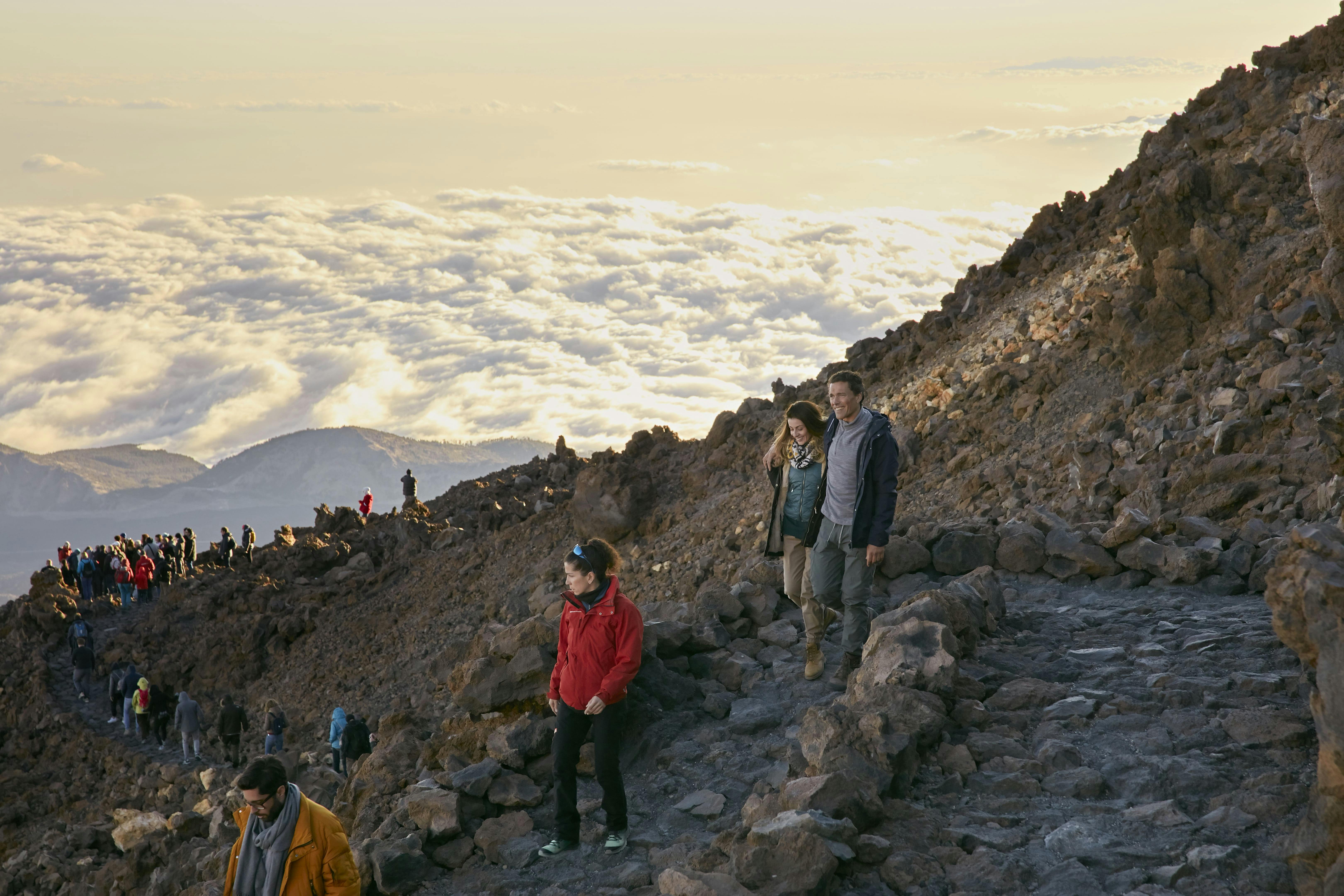 日落时分，三个人在岩石山路上徒步旅行，下面是云海。