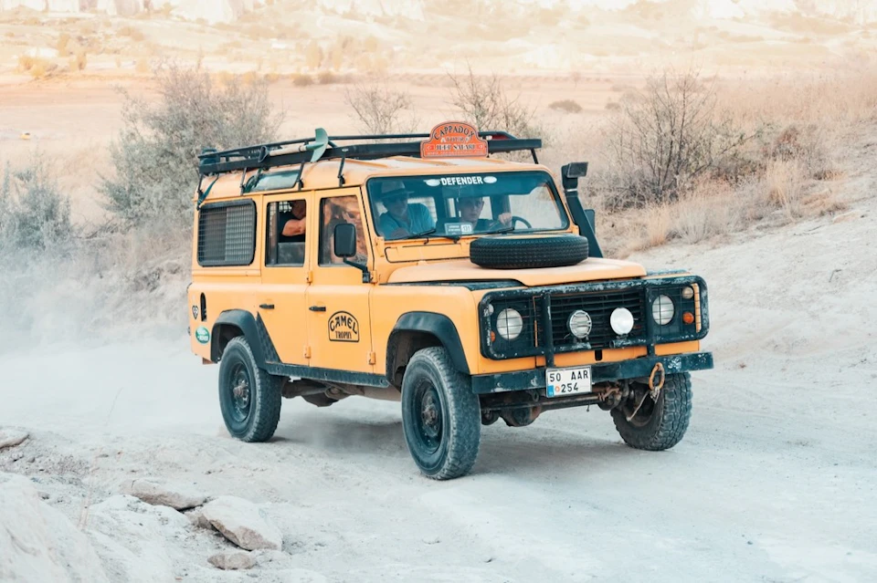 A yellow off-road vehicle driving on a dirt path in a desert-like environment with sparse vegetation.