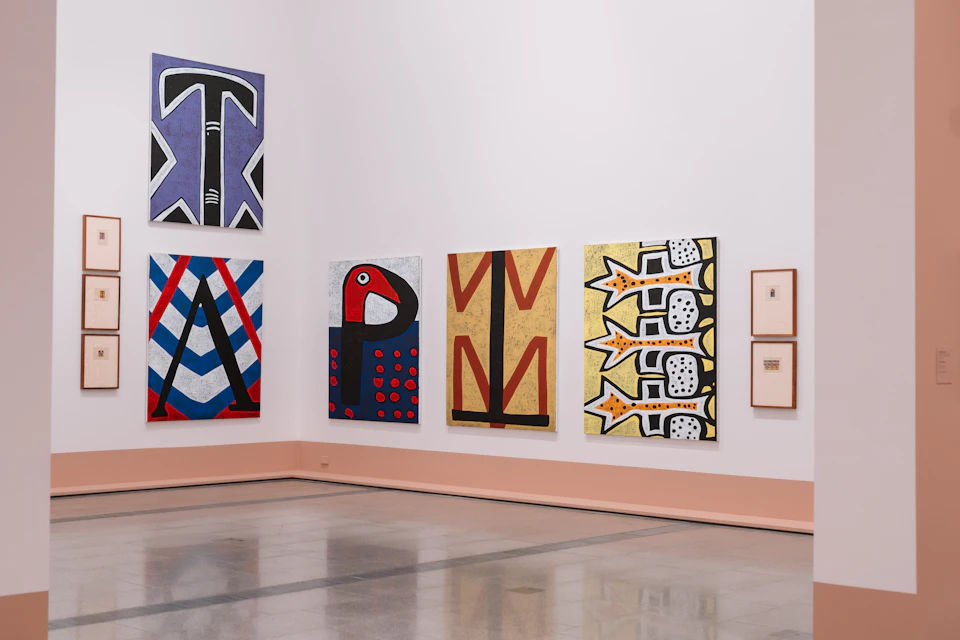 A gallery wall with colorful abstract paintings and framed works displayed on a polished floor.