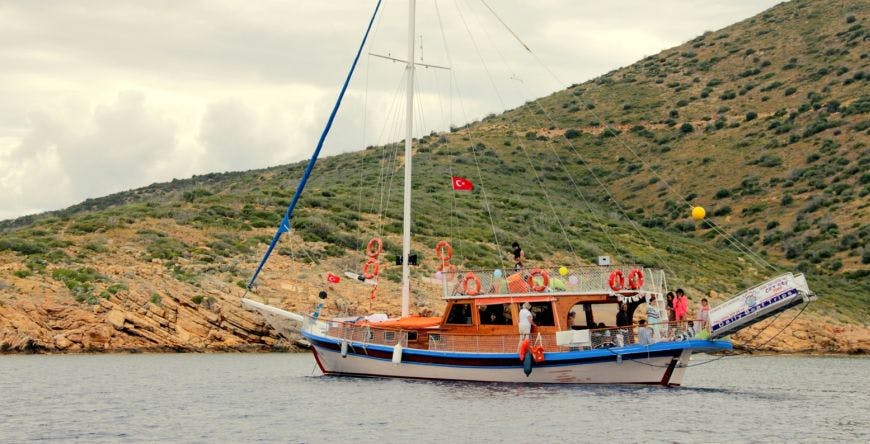 바위가 많고 언덕이 많은 해안선 근처에 터키 국기가 달린 범선이 정박해 있습니다.