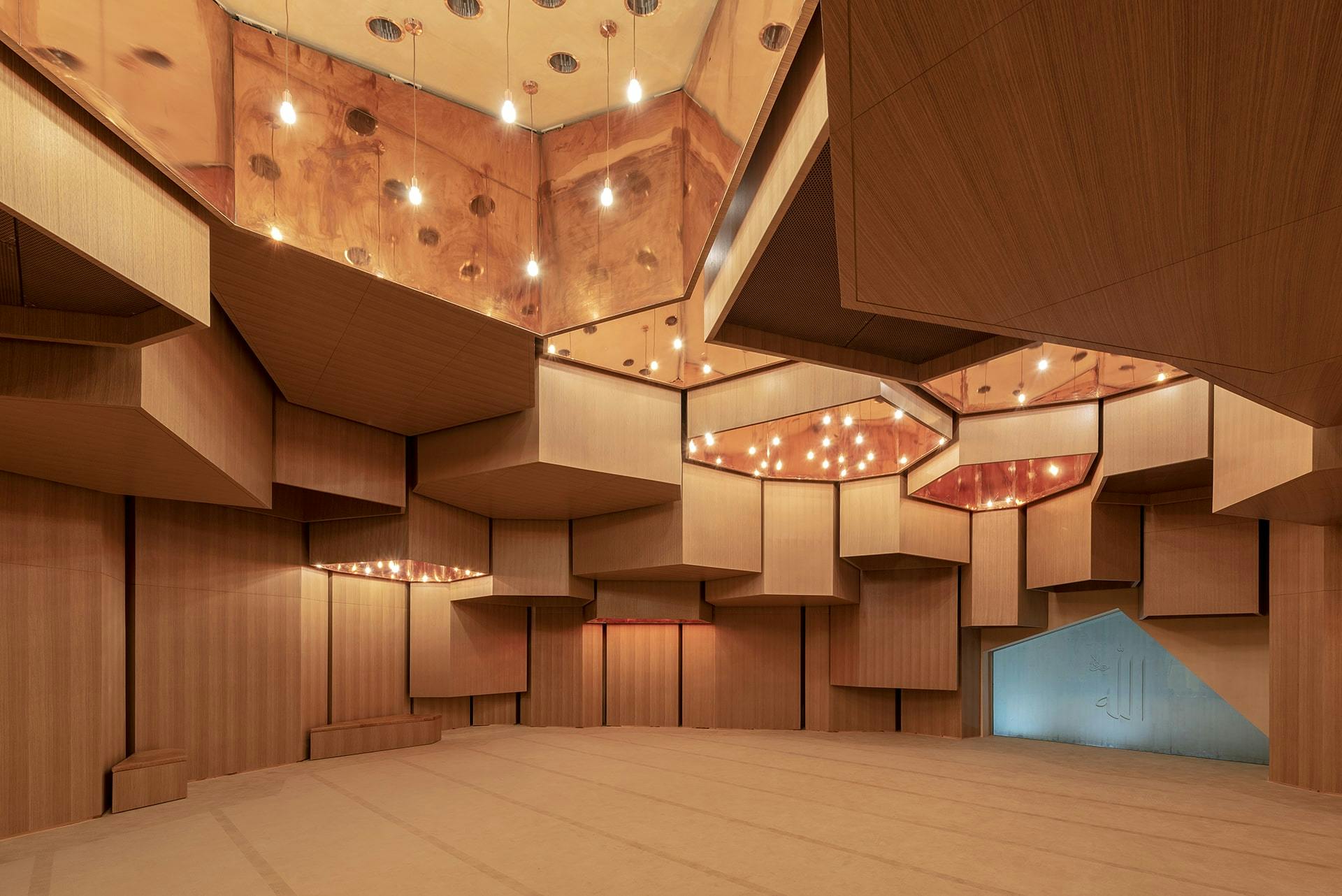 A modern room with geometric wooden panels, mirrored ceiling, and multiple hanging lights. The space is empty.