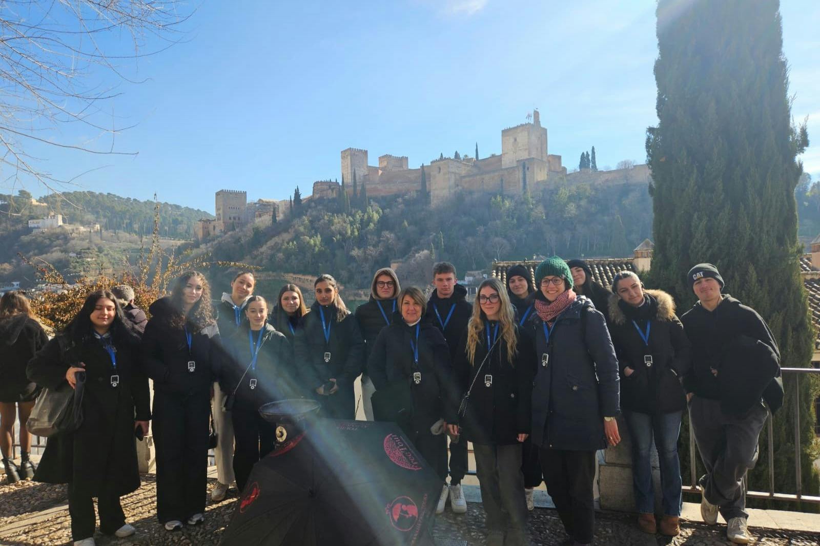 Eine Gruppe von Menschen posiert im Freien mit einer historischen Burg auf einem Hügel im Hintergrund unter einem klaren Himmel.