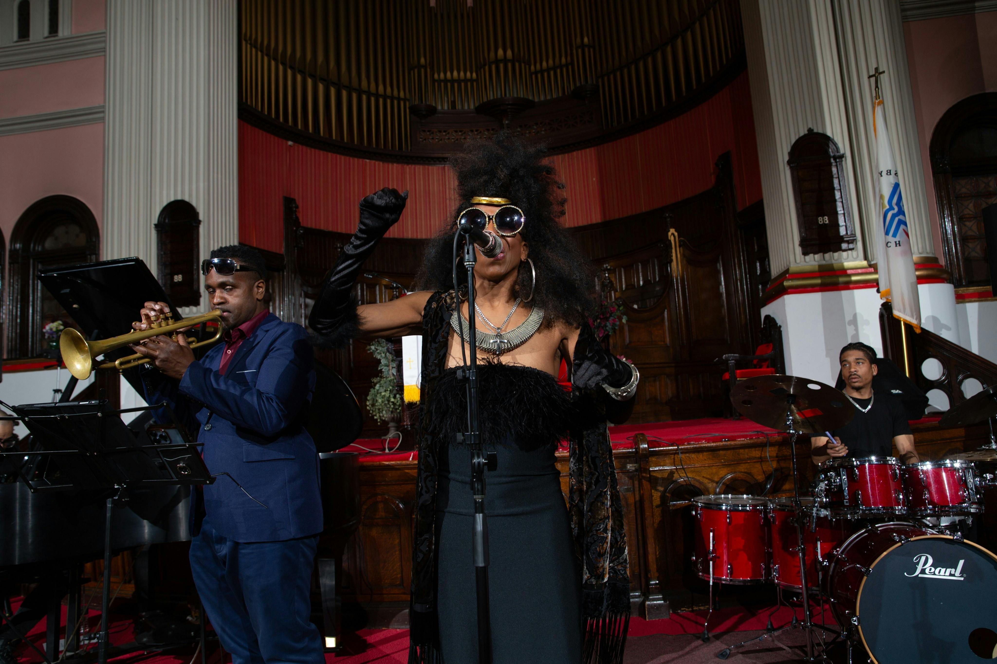 음악가가 트럼펫을 연주하고 가수가 나무 오르간 배경이 있는 교회에서 마이크를 잡고 연주합니다.