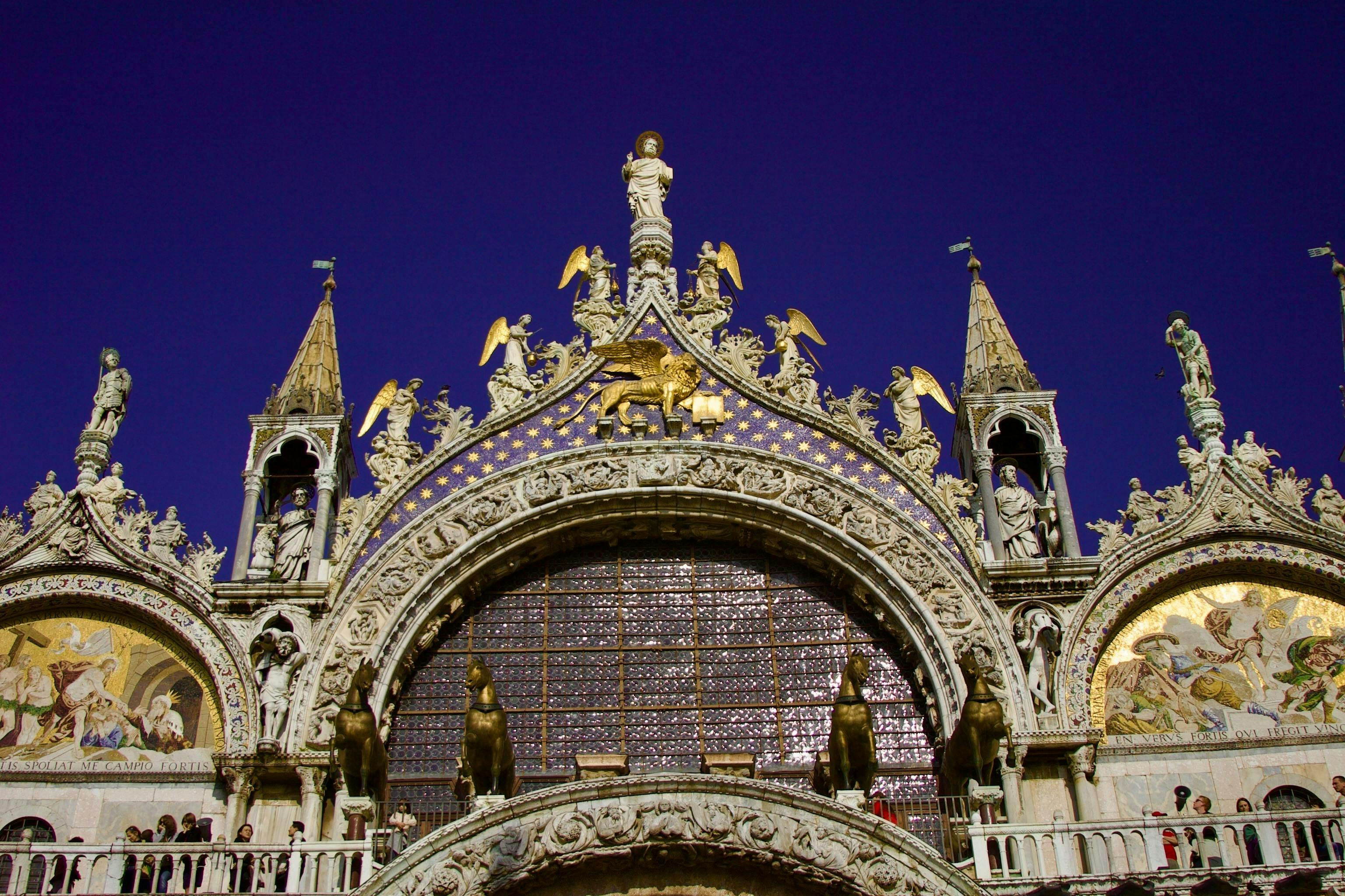 Elaborate facade of a historical building with arched windows, statues, and golden accents against a deep blue sky.