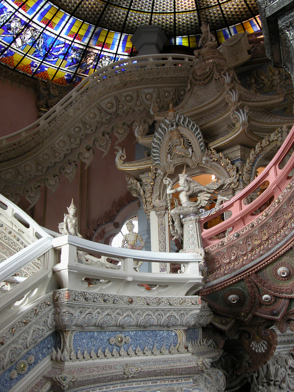 Ornate and intricately decorated staircase, detailed with sculpted figures and lavish designs, beneath a stained glass dome.