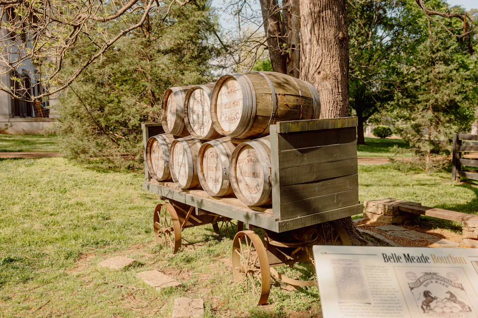Wooden cart with six barrels in a grassy area, surrounded by trees. An information plaque is in the foreground.