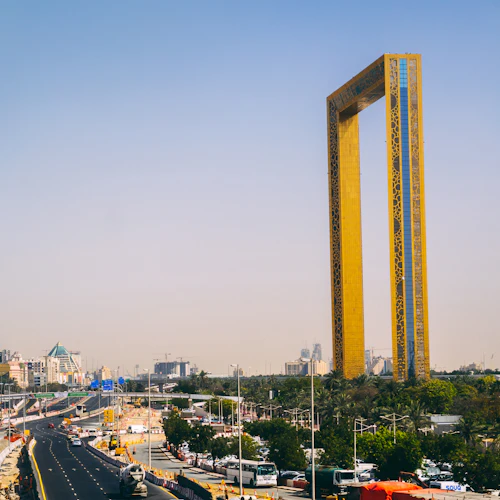 A large rectangular yellow frame structure stands tall amidst a cityscape with buildings, roads, and light traffic.