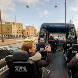 Turister i en öppen buss i en stad som tar foton av landmärken och byggnader. Ett museum syns i bakgrunden.