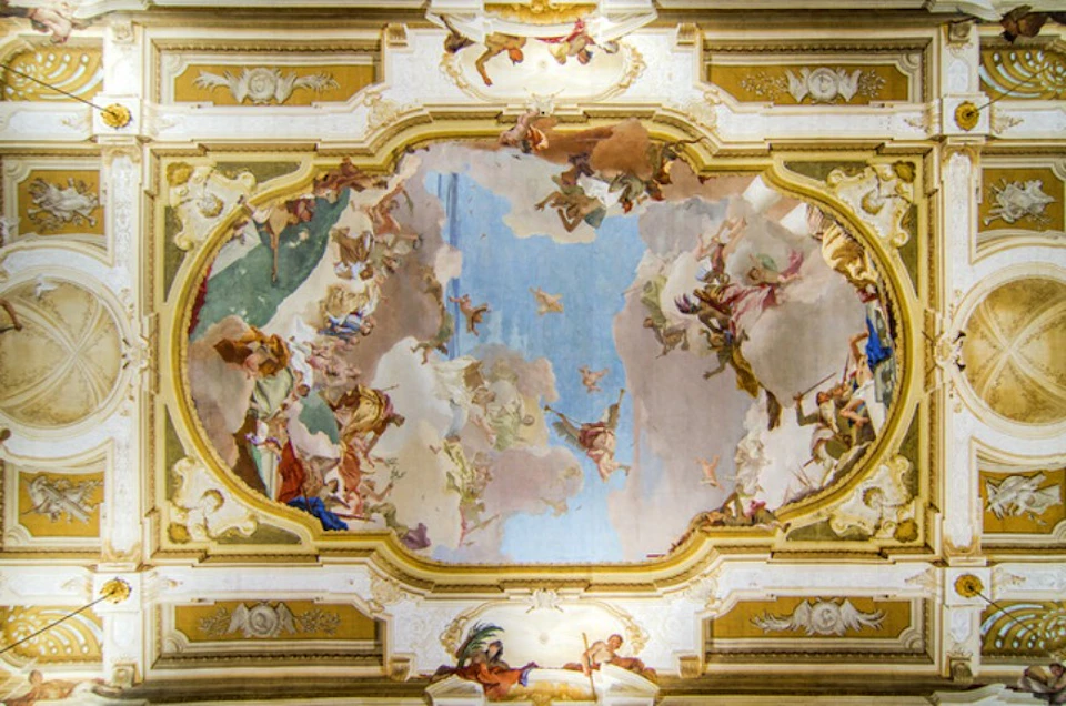 Baroque ceiling fresco featuring figures and clouds, surrounded by intricate gold and white architectural details.