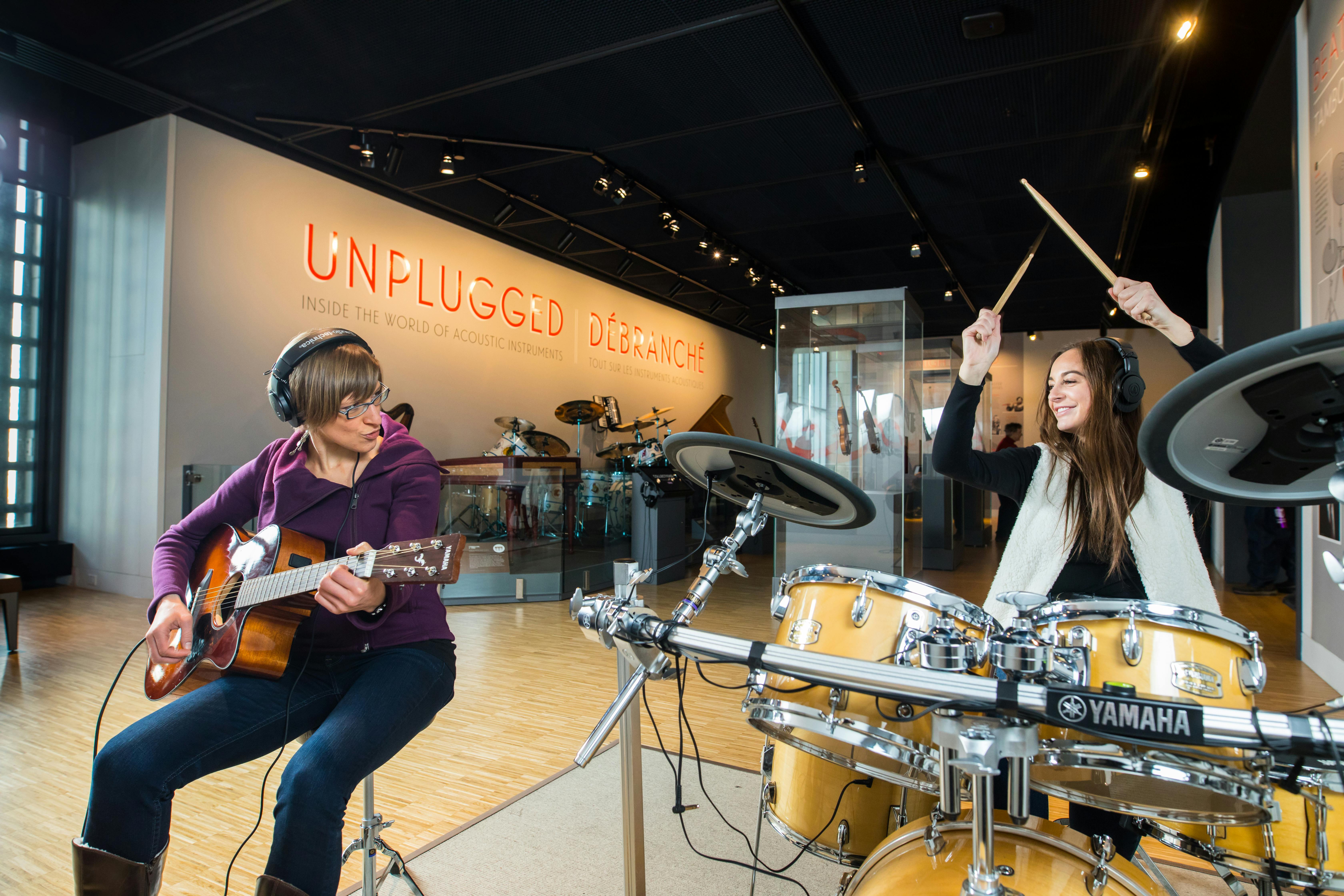 Persona che suona una chitarra con gli Auricolari in una mostra musicale. Sullo sfondo una batteria e un cartello con la scritta "Unplugged".