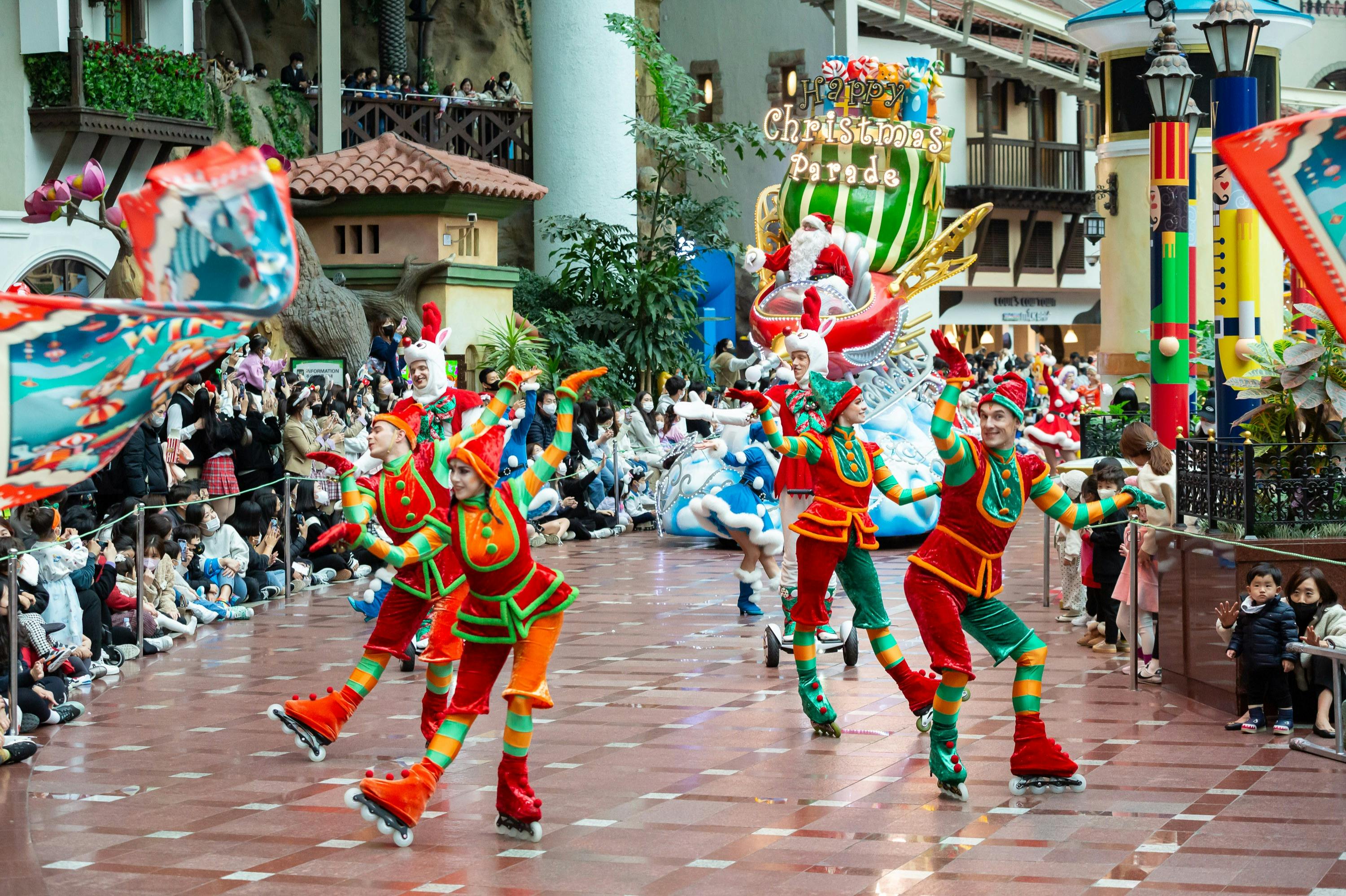 お祝いの衣装とローラースケートを着た人々、そりに乗ったサンタ、横から見ている見物人が参加するカラフルなクリスマスパレード。