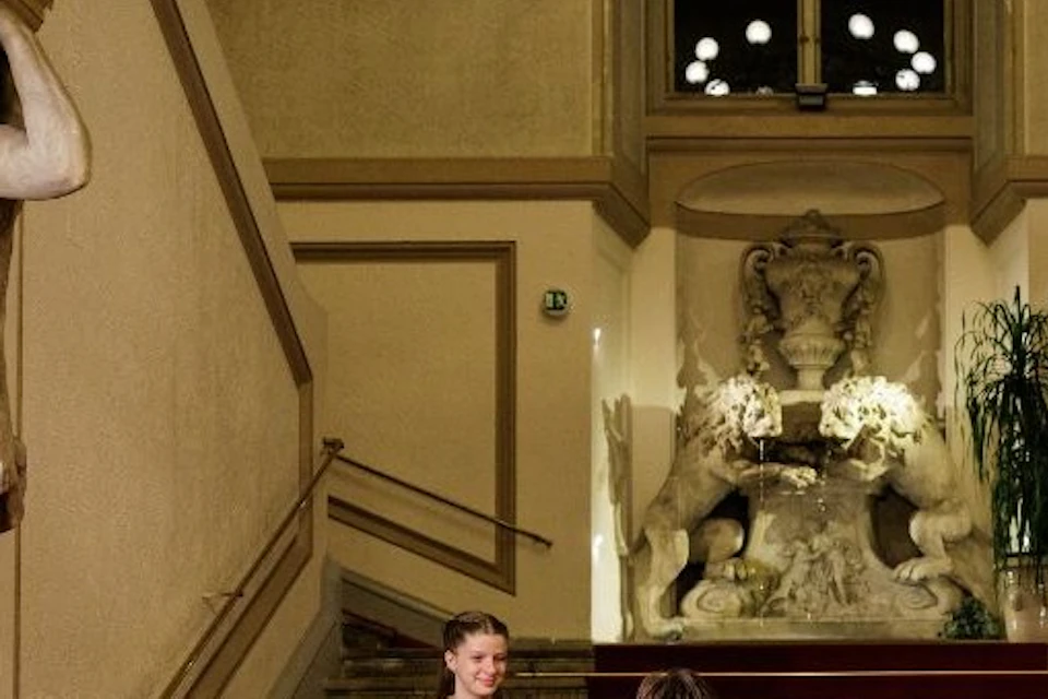A group of people dressed in formal and historical attire ascending a red-carpeted staircase in an ornate interior setting.