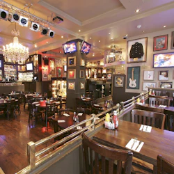 Rymlig restaurang med träbord och stolar, inramade musikminnen, ljuskronor, TV-skärmar och ett barområde i bakgrunden.