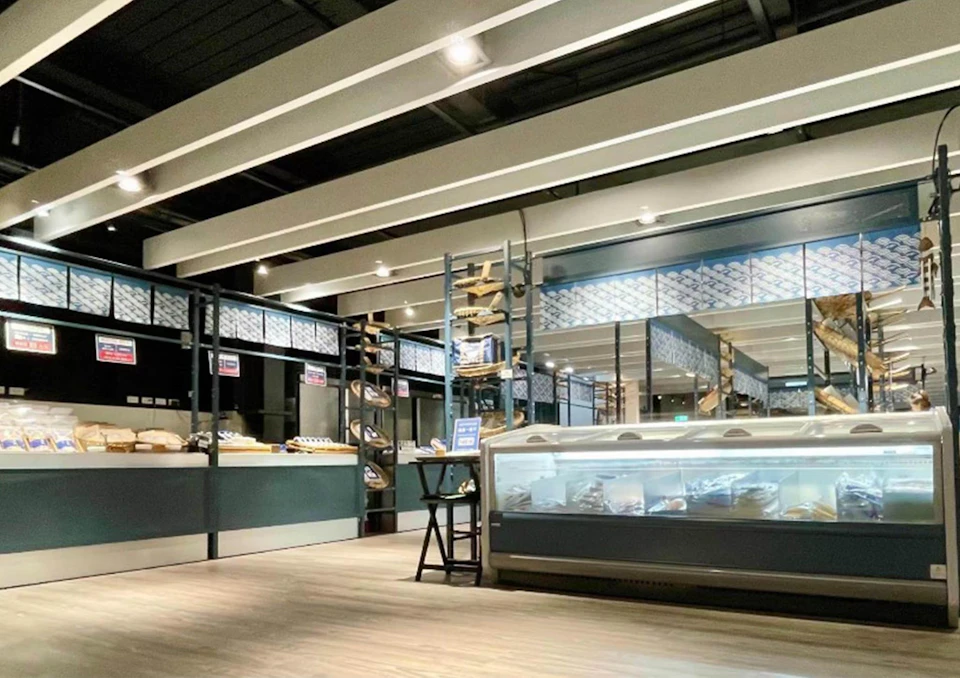 Modern bakery interior with shelves of bread and a glass display case under bright ceiling lights.