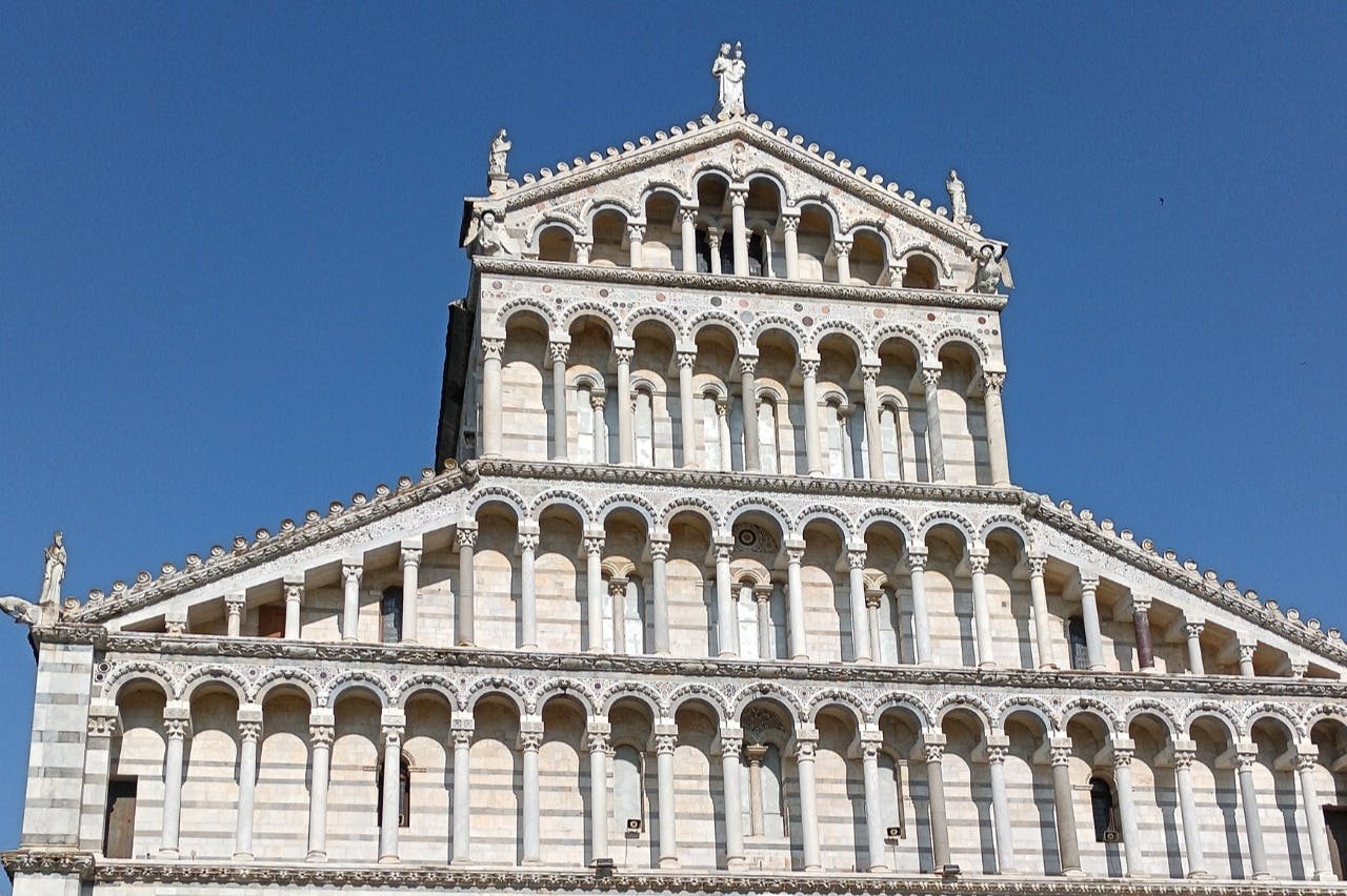 Η περίτεχνη πρόσοψη ενός ιστορικού κτιρίου με πολλαπλές σειρές από καμάρες και αγάλματα με φόντο έναν καταγάλανο ουρανό.