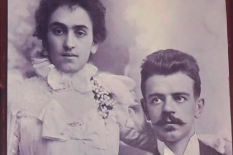 Ένα βίντατζ πορτρέτο μιας γυναίκας με λευκό δαντελένιο φόρεμα και ενός άνδρα με μουστάκι, που κοιτάζουν κατευθείαν την κάμερα.