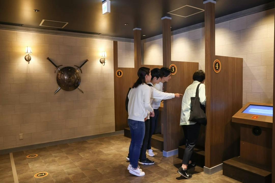 People interacting with numbered wooden booths in a room decorated with medieval-themed elements and warm lighting.